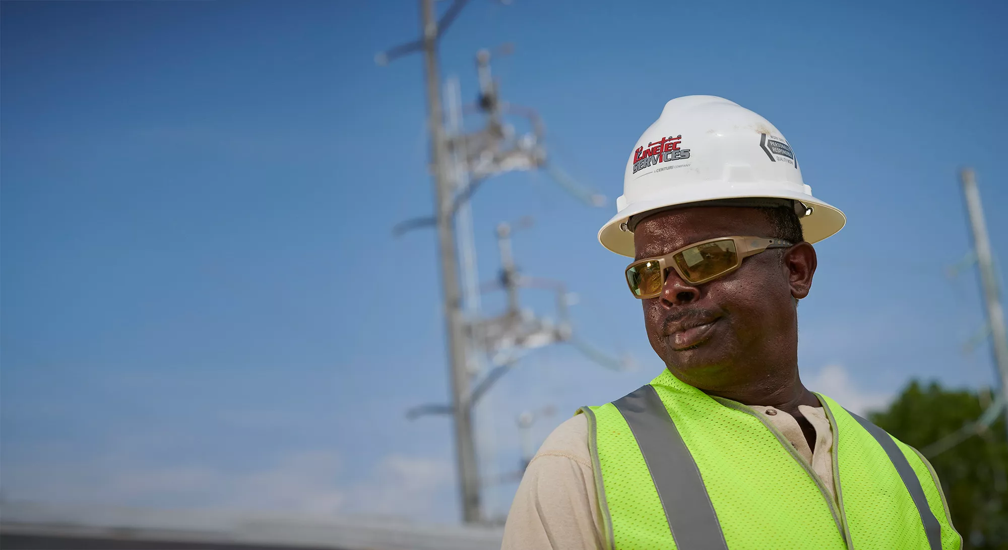 A man of color wearing a Linetec hard hat looks out over power lines.