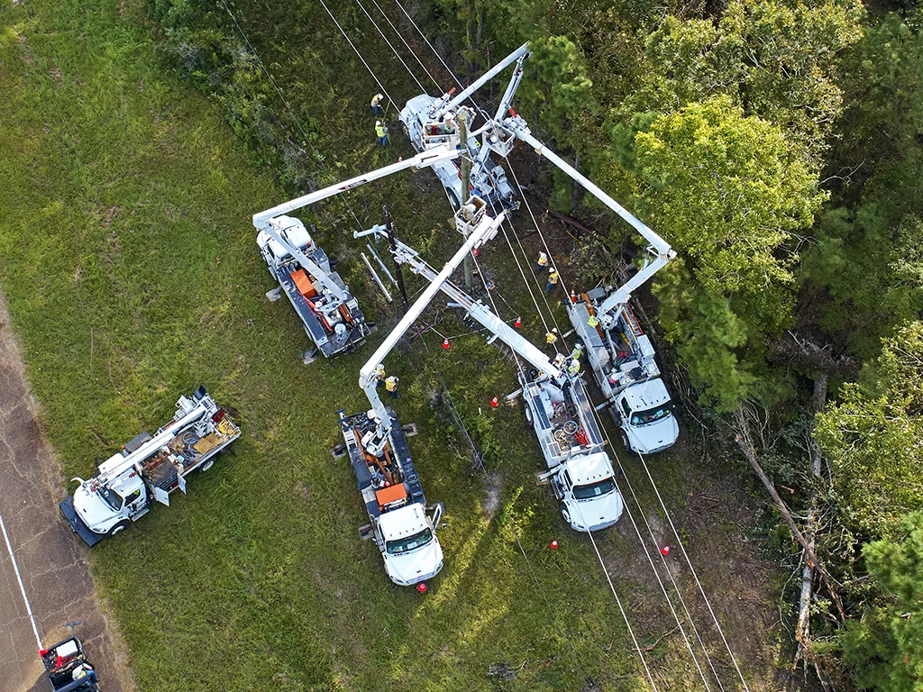 Viewed from above, Linetec trucks work on power lines in a green field.